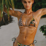Woman in a colorful bikini standing on a beach with palm leaves in the background
