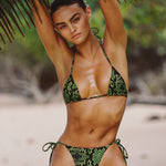 Woman in a green bikini sitting under a palm tree on a beach