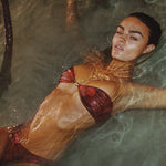 Woman in a red bikini lying in water with mangrove roots in the background